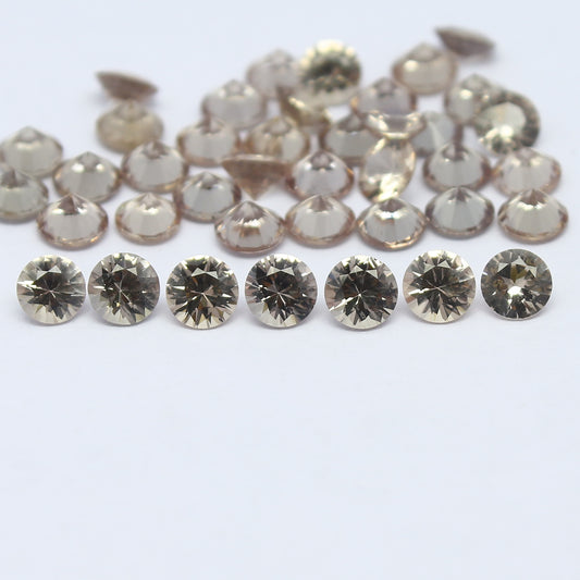 A collection of round shape diamond cut faceted gemstones, appears beige in color, arranged in rows on a white surface.